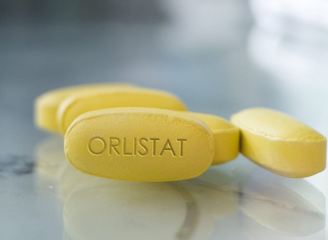Orlistat yellow pill on glass background drug medication designed to treat obesity and prevent absorption of fats from human diets by acting as a lipase inhibitor