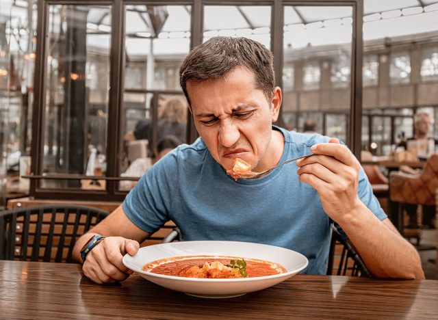 dissatisfied unhappy customer of the restaurant sniffs the disgusting smell of a bowl of soup with spoiled ingredients and is going to complain to the chef