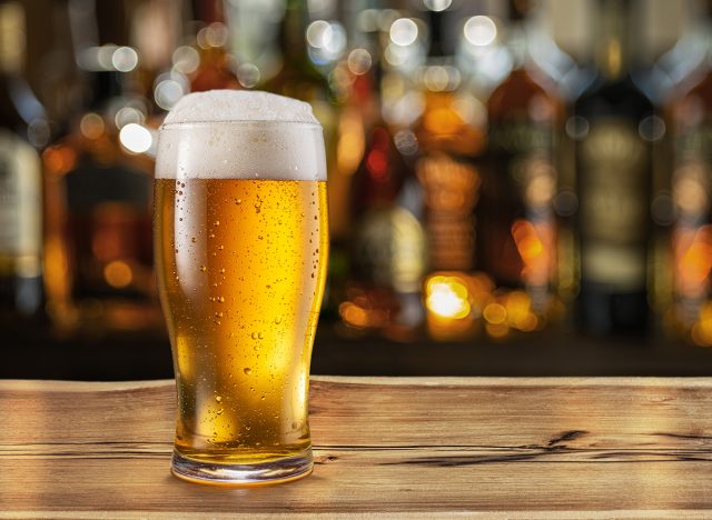 Glass of chilled beer on table and blurred sparkling bar background.