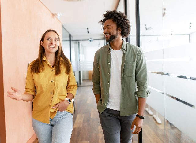 Couple of business people discussing tasks walking in the office hall. Two diverse colleagues have small talk during break. Friendly atmosphere in team