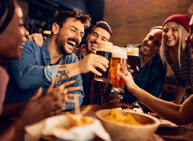 Multiracial group of happy friends having fun while toasting with beer in a bar.