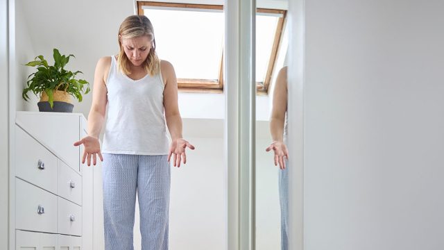 Menopausal Mature Woman Concerned With Weight Gain Standing On Scales In Bedroom At Home