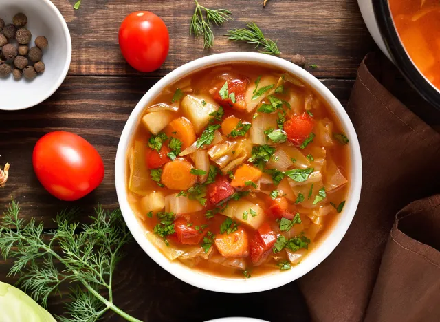 Vegetable cabbage soup in bowl over wooden background. Top view, flat lay