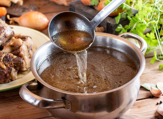 Saucepan with bouillon with a ladle on rustic wooden table. Bone broth