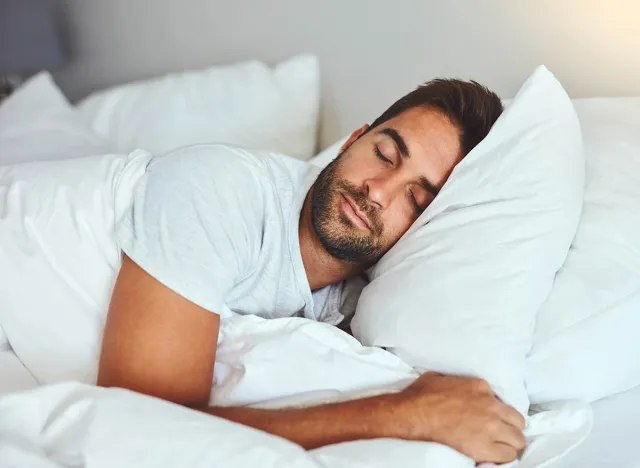 Man, sleeping and bed in morning rest for healthy wellness, peace and quiet on comfort pillow at home. Tired or exhausted male person asleep or dreaming on peaceful holiday or weekend in the bedroom