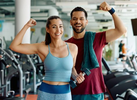 Happy athletic couple flexing their muscles after working out in a gym and looking at camera.