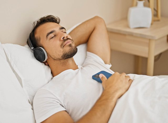 Young hispanic man listening to music relaxed on bed at bedroom