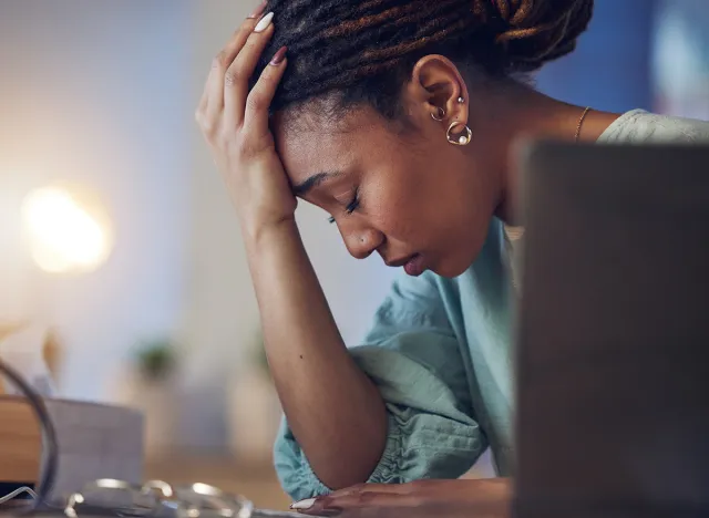 Business woman, depression and stress in an office at night working late on deadline. Tired African entrepreneur person with hands on head for pain, burnout or regret for mistake or fail at work