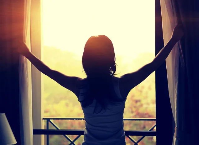 young woman opening curtains in a bedroom