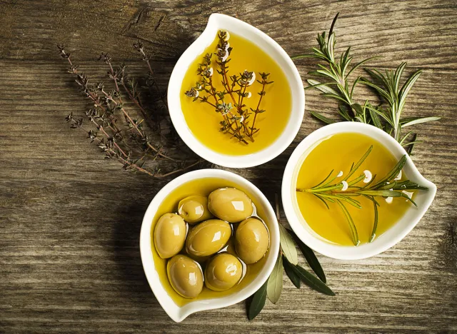 Olive oil with fresh herbs on wooden background.