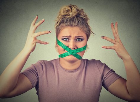 New diet restriction and stress concept. Portrait of young frustrated woman with a green measuring tape around her mouth isolated gray background. Human face expression emotion. Healthy lifestyle
