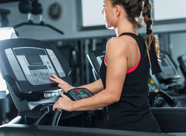 Young female athlete exercising on treadmill in modern gym, setting up difficulty level.