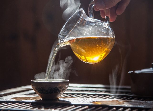 Hand that pours chinese green tea from glass kettle to smal cup