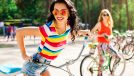 Outdoor lifestyle portrait of two best friends hipster girls wearing stylish bright outfits, denim shorts and glasses going crazy and having great time together. Laughing and ride bikes
