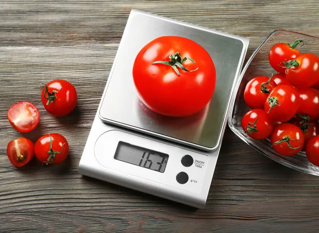 Tomatoes with digital kitchen scales on wooden background