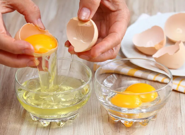 Woman hands breaking an egg to separate egg white and yolks and egg shells at the background