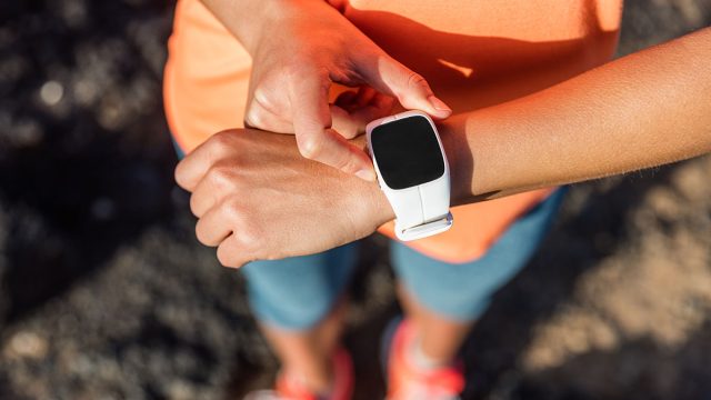 Trail runner athlete using her smart watch app to monitor fitness progress or heart rate during run cardio workout. Woman training outdoors on mountain rocks. Closeup of tech gear.