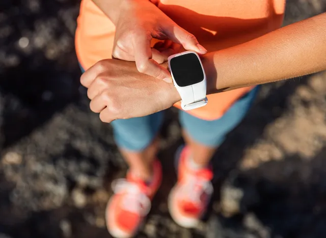 Trail runner athlete using her smart watch app to monitor fitness progress or heart rate during run cardio workout. Woman training outdoors on mountain rocks. Closeup of tech gear.