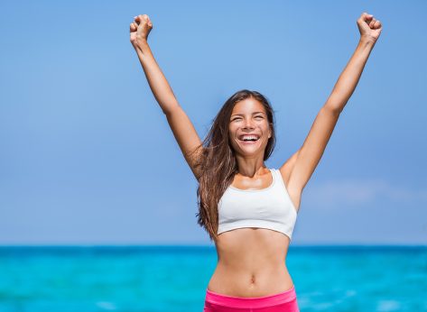 Happy fitness success woman winner. Asian girl cheering arms up of joy on summer beach.