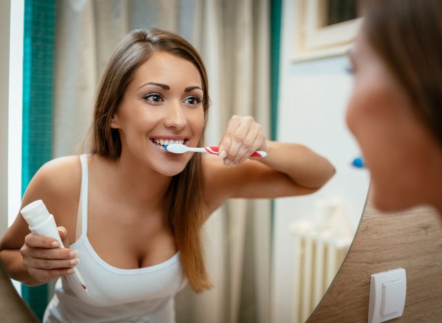 Beautiful young woman brushing teeth in front of her bathroom mirror. Selective focus.