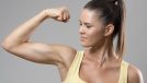 Strong sporty fit woman in yellow tank top flexing bicep muscle over gray studio background.