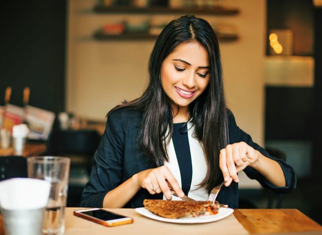 A happy young Indian woman having a pancake in a restaurant