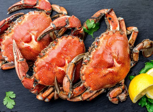 Cooked crabs on black plate served with white wine, black slate background, top view.