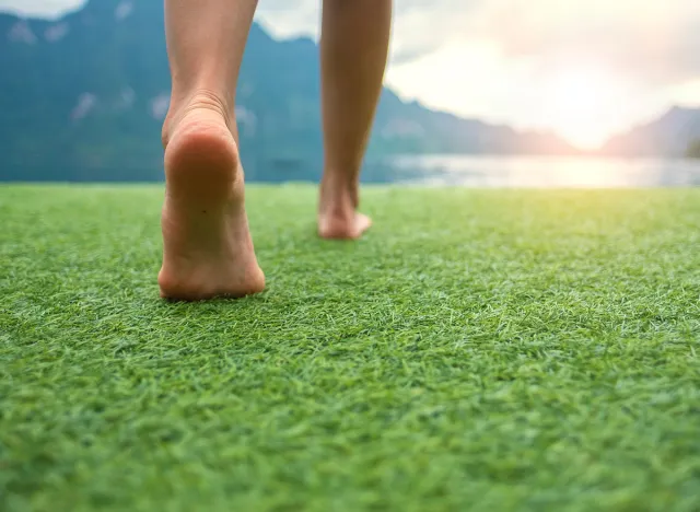 Young female legs walking towards the sunset on a ground grass with blur mountain and lake