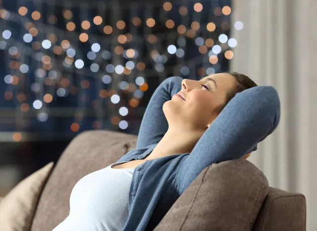 Side view portrait of a relaxed happy woman resting sitting on a couch in the night at home