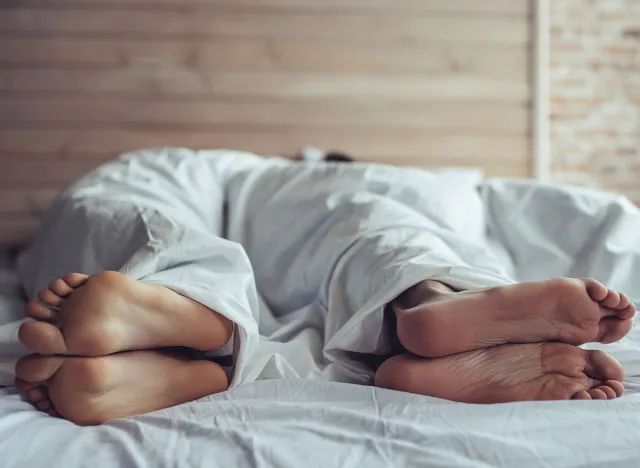 Beautiful young couple in bedroom. Close up of male and female feet under the blanket looking away from each other.