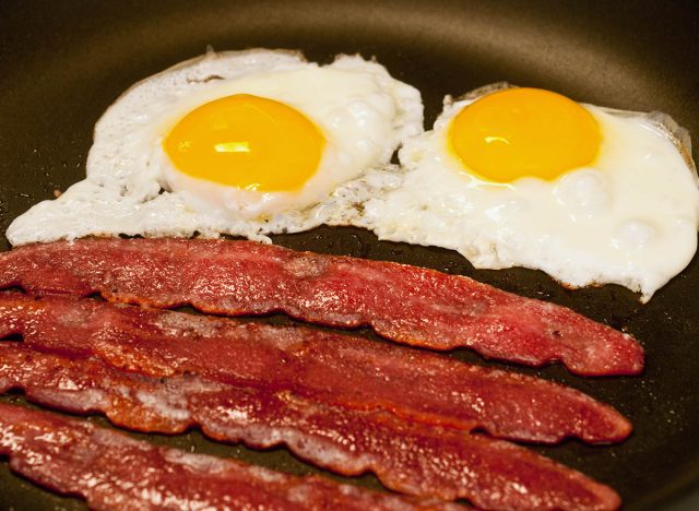 Fried eggs and bacon cooking in a skillet