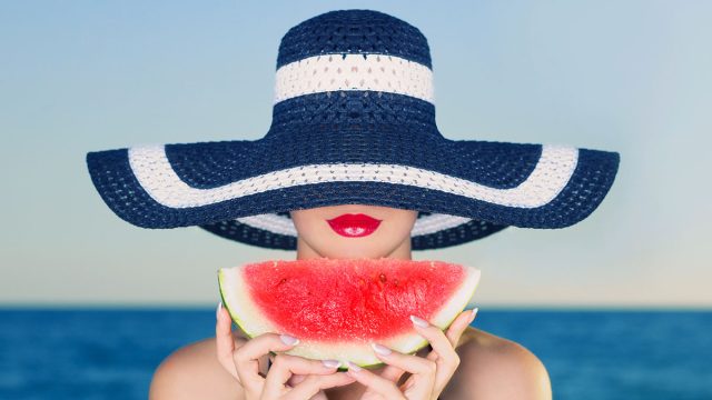 Young stylish lady in a hat at sea with watermelon