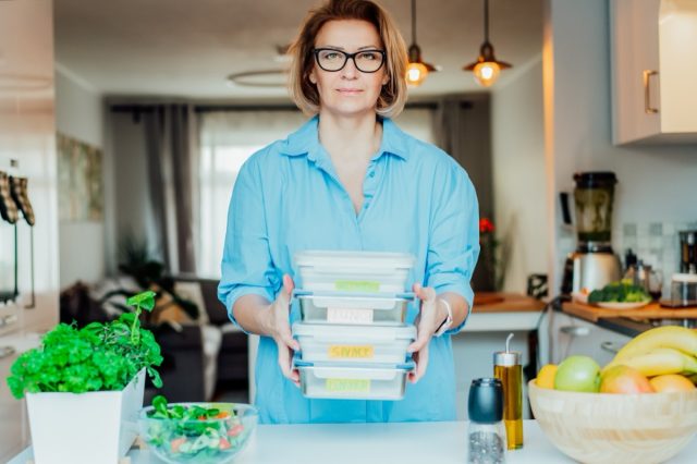 Healthy diet plan for weight loss, daily ready meal menu. Woman holding lunch boxes just cooked in advance, ready to be served. Containers with eco healthy food. Pre-cooking concept. Selective focus.