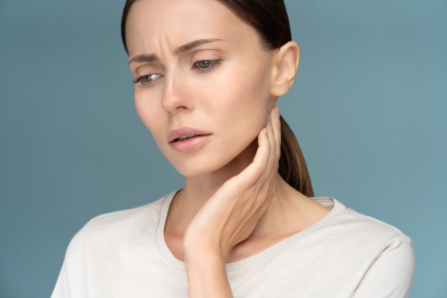 Closeup of sick sad woman checking lymph nodes, caught cold, suffering from throat problems.