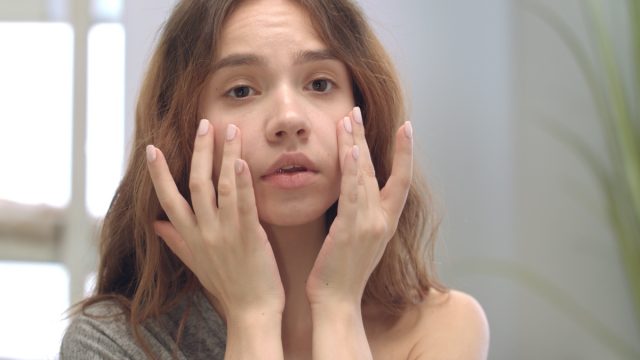 Dissatisfied woman touching face skin front bathroom mirror.