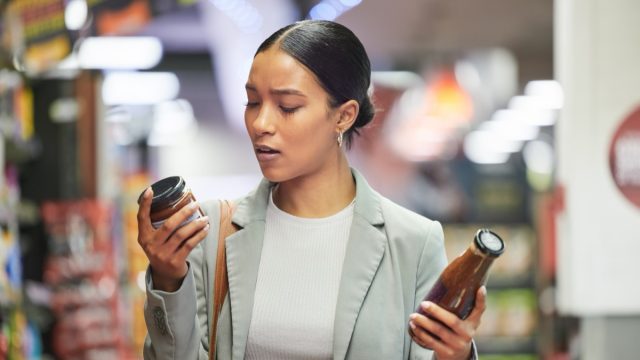 Woman in a store or supermarket, reading product labels of choice to decide or compare sauce bottles.