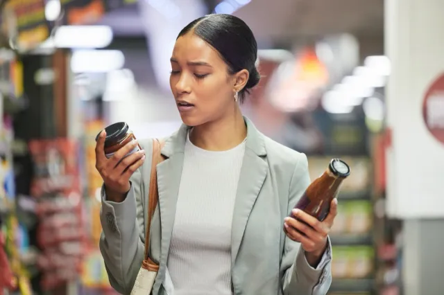 Woman in a store or supermarket, reading product labels of choice to decide or compare sauce bottles.