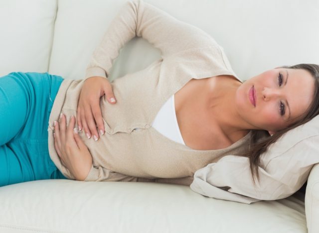 Woman lying on the sofa in the living room with upset stomach