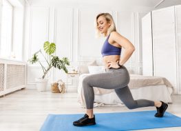 Athletic woman in stylish sportswear doing lunges exercises at home in bedroom.