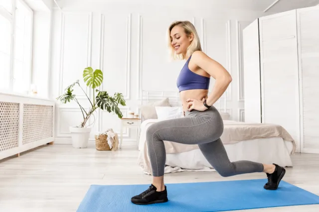 Athletic woman in stylish sportswear doing lunges exercises at home in bedroom.