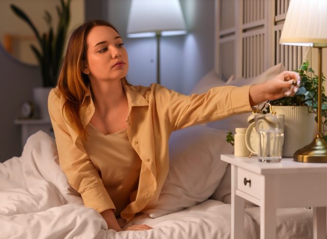 Young woman turning off lamp before sleep in bedroom.
