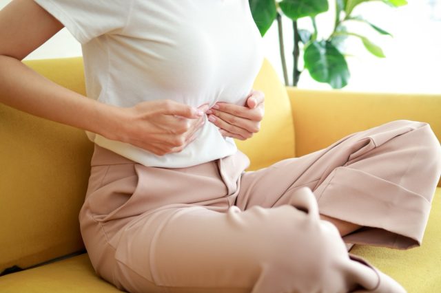 Woman with abdominal pain in the middle above the navel. She sits on the sofa at home.