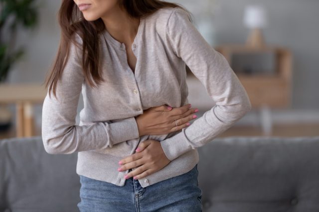 Woman standing holding belly suffering from stomach pain.