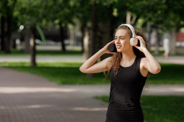 young attractive woman listening to music on headphones in summer park