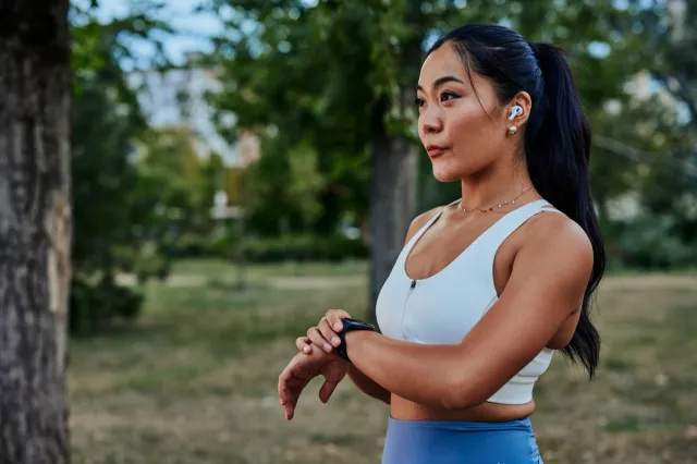 Asian woman setting up the fitness smartwatch for running. Sportswoman checking watch device during workout in park