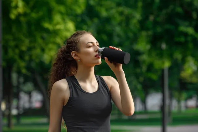 young attractive woman drinks water after running in summer park