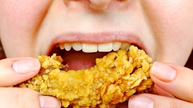 Woman eating a takeaway fried chicken wing from fast food cafe with a mouth and teeth close up