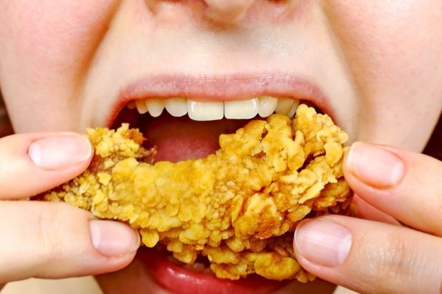 Woman eating a takeaway fried chicken wing from fast food cafe with a mouth and teeth close up