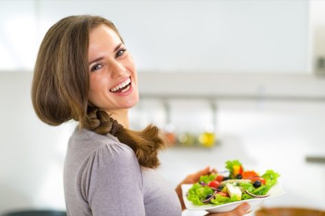 Portrait of happy young housewife with greek salad.