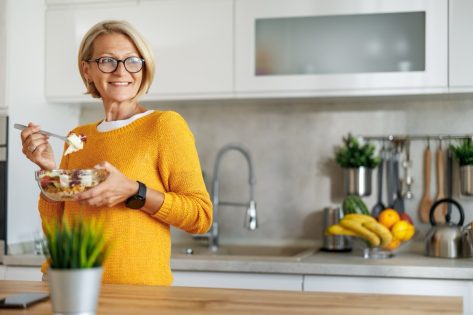 Mature woman eating salad at home.